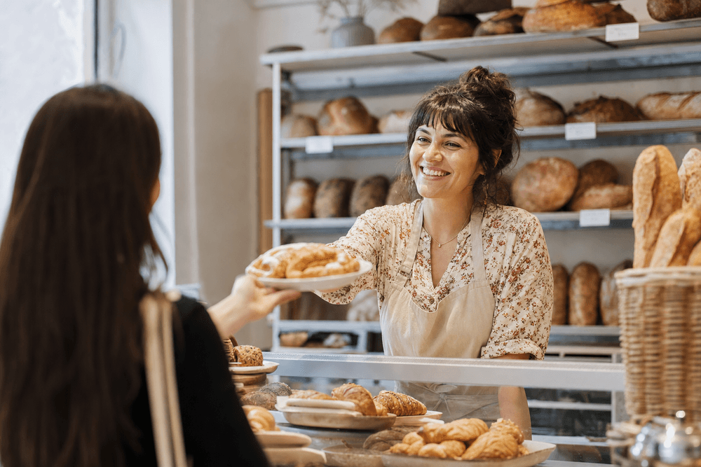 A new-bakery owner greeting a first-time customer warmly across the counter.