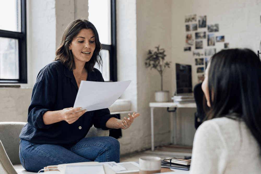 A copywriter-agency owner reading a draft aloud to a colleague in a bright studio.