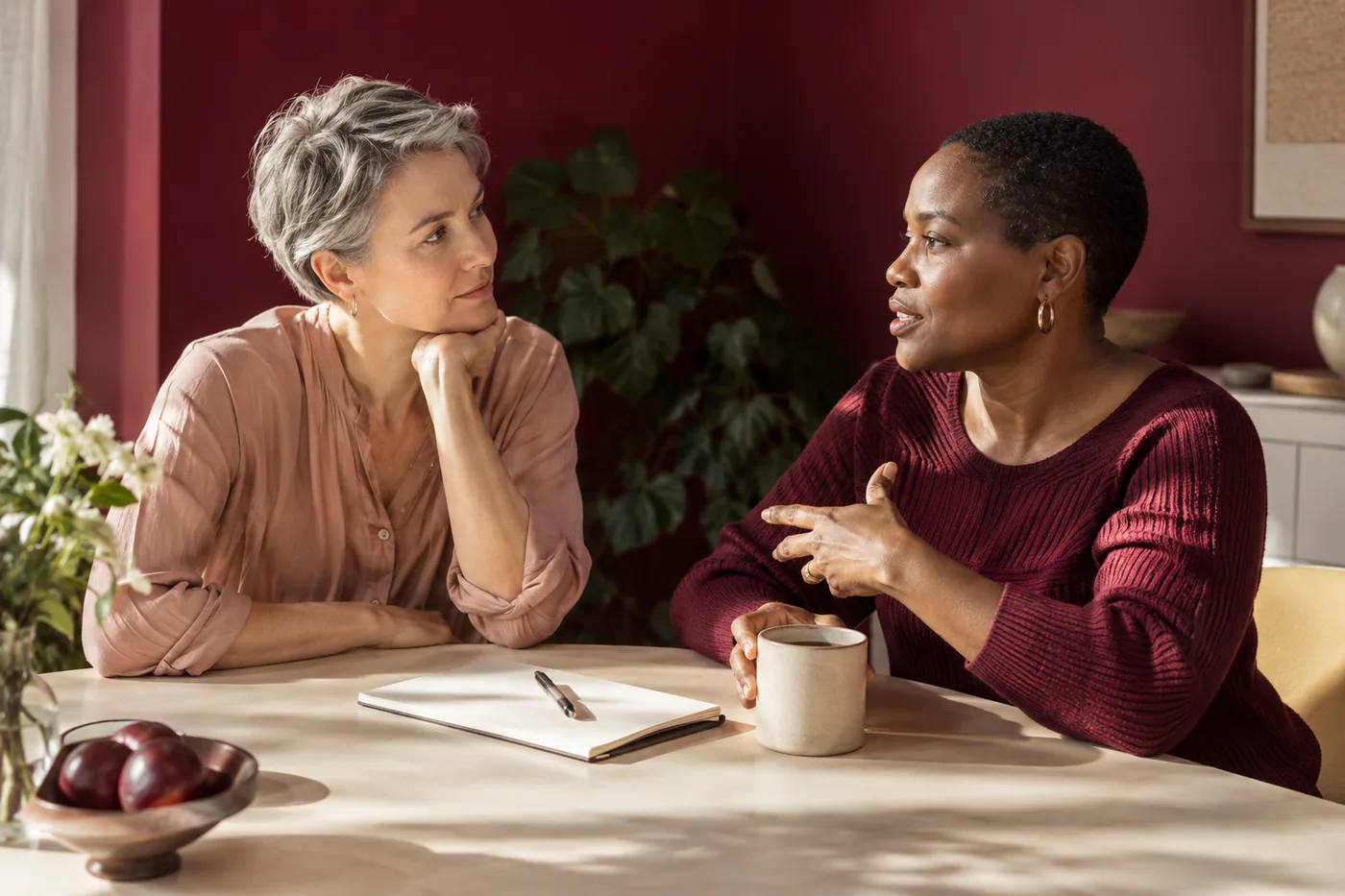 Two women talking at a table with an open blank notebook
