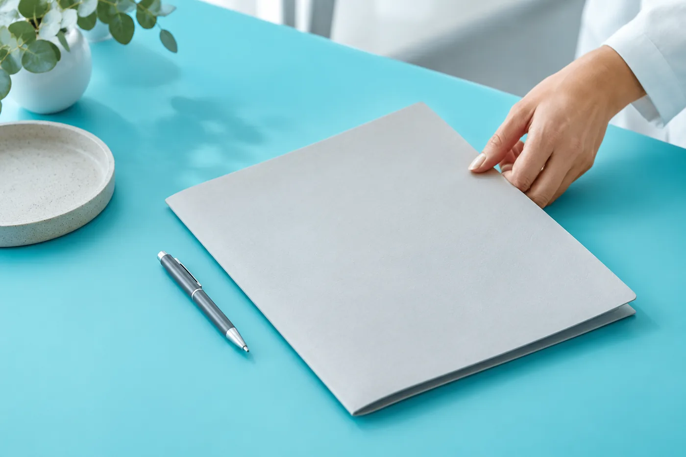 A hand arranging a closed folder and pen on a cyan desk