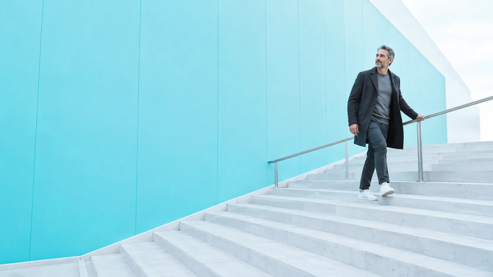 An adult using a broad sunlit staircase beside a cyan architectural panel