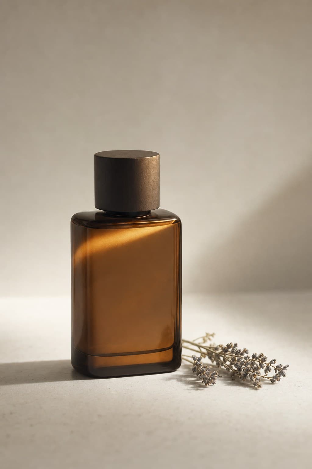 A minimalist amber fragrance bottle on porcelain beside a sprig of dried botanicals.