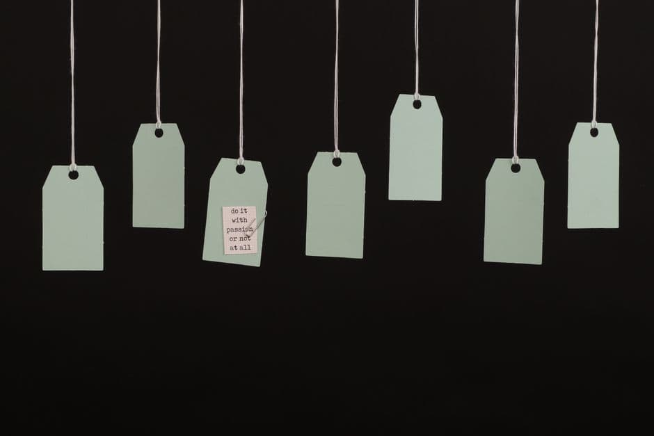A row of pale sage-green price tags hanging on strings against a black background, one bearing a small typed note.