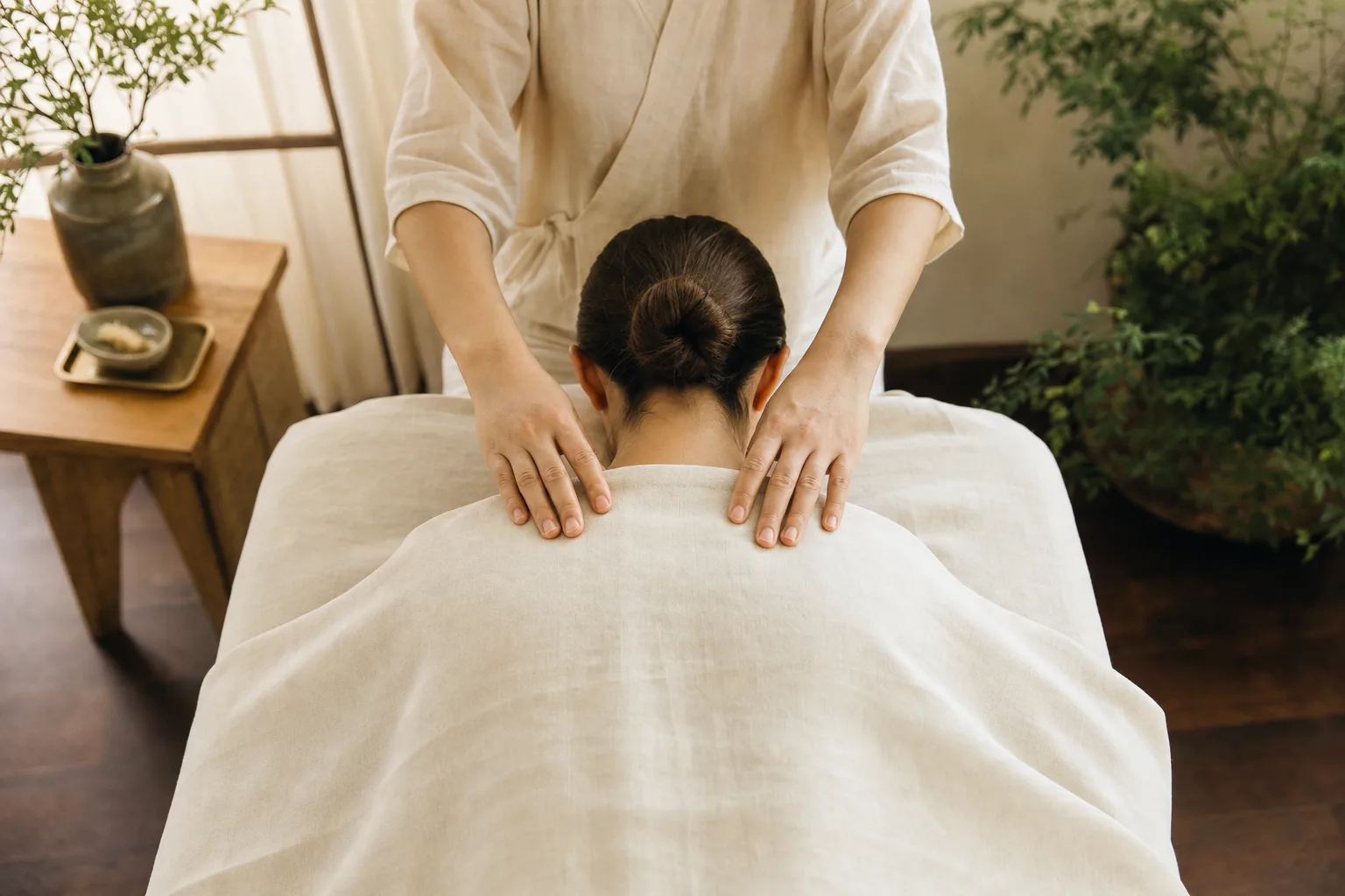 Calm hands performing slow tui na bodywork on a draped upper back
