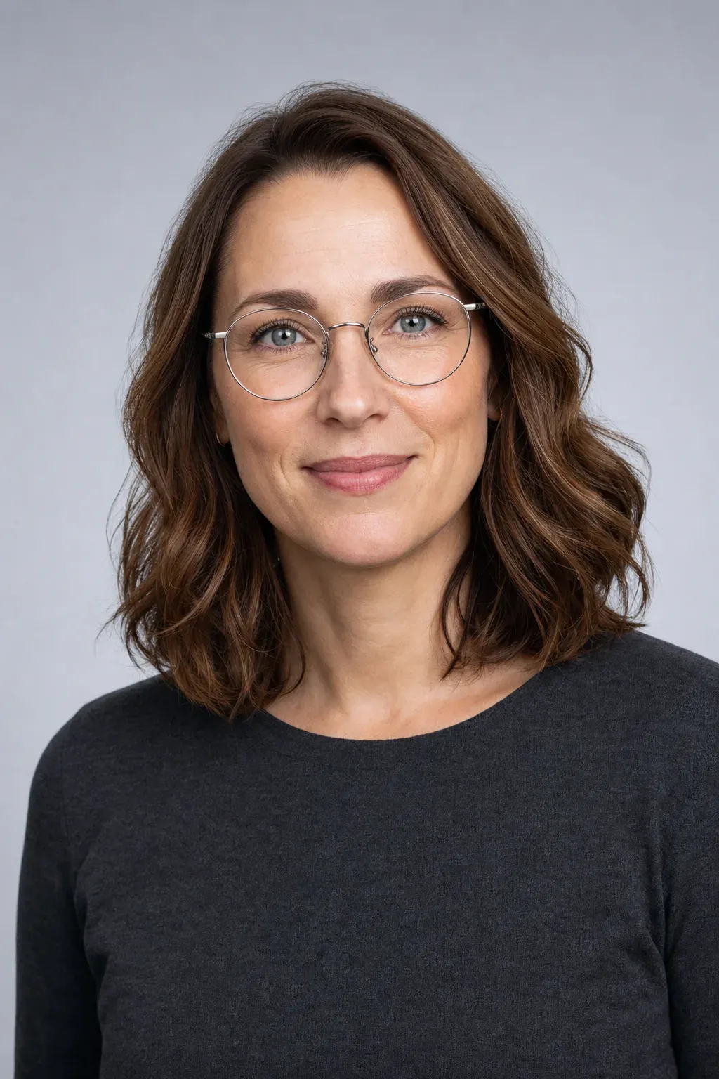 Dr. Nora Kessler, optometrist and founder, in round thin-rim glasses against a cool grey backdrop.
