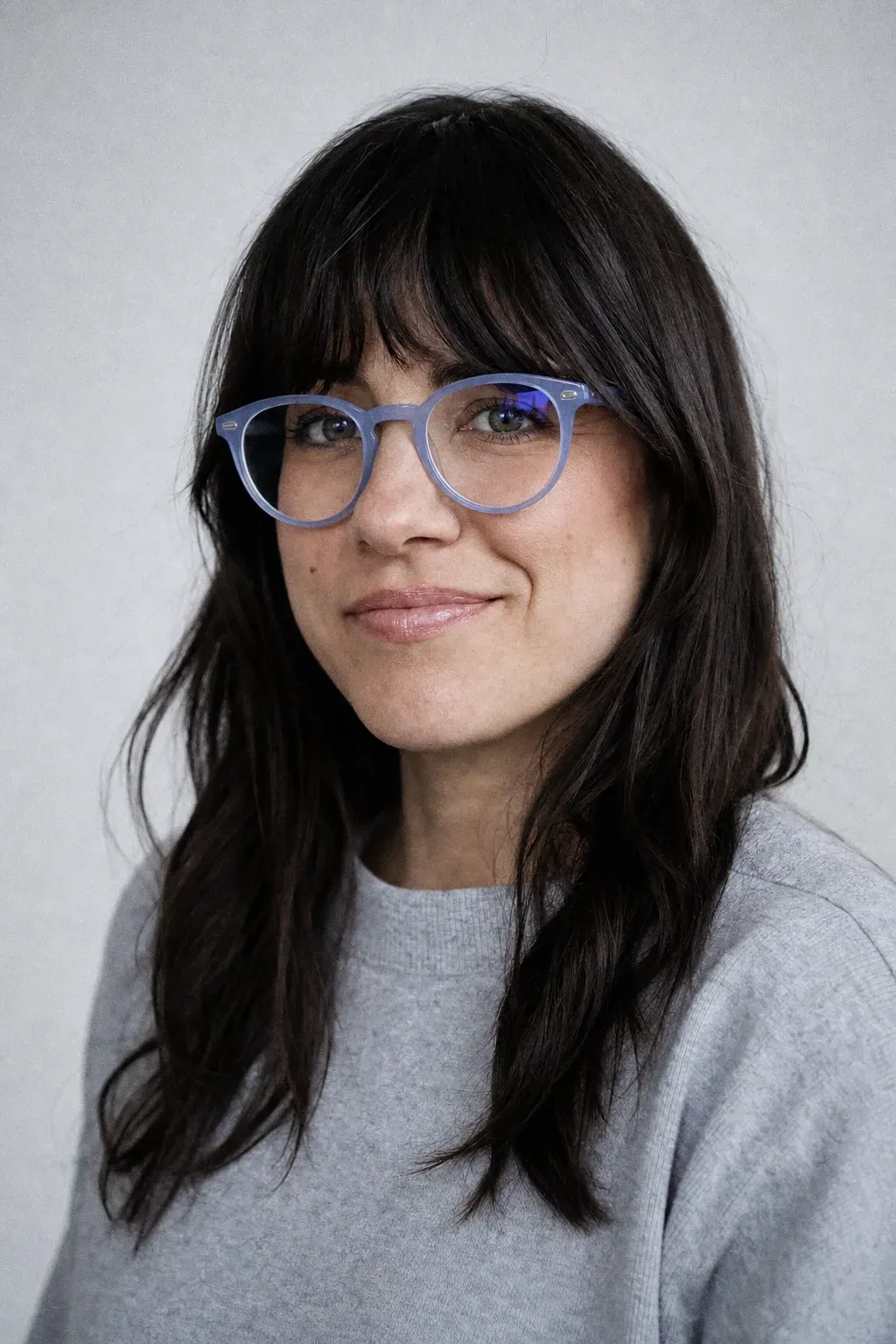 Portrait of a smiling woman, soft daylight, plain background.