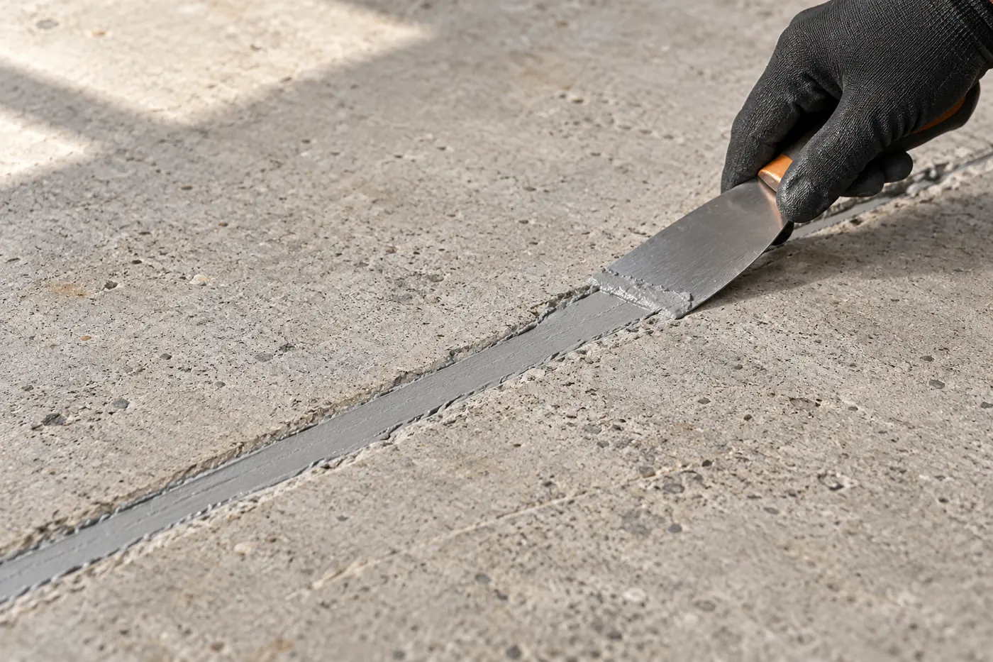 A gloved hand smoothing polymer filler into a prepared concrete crack